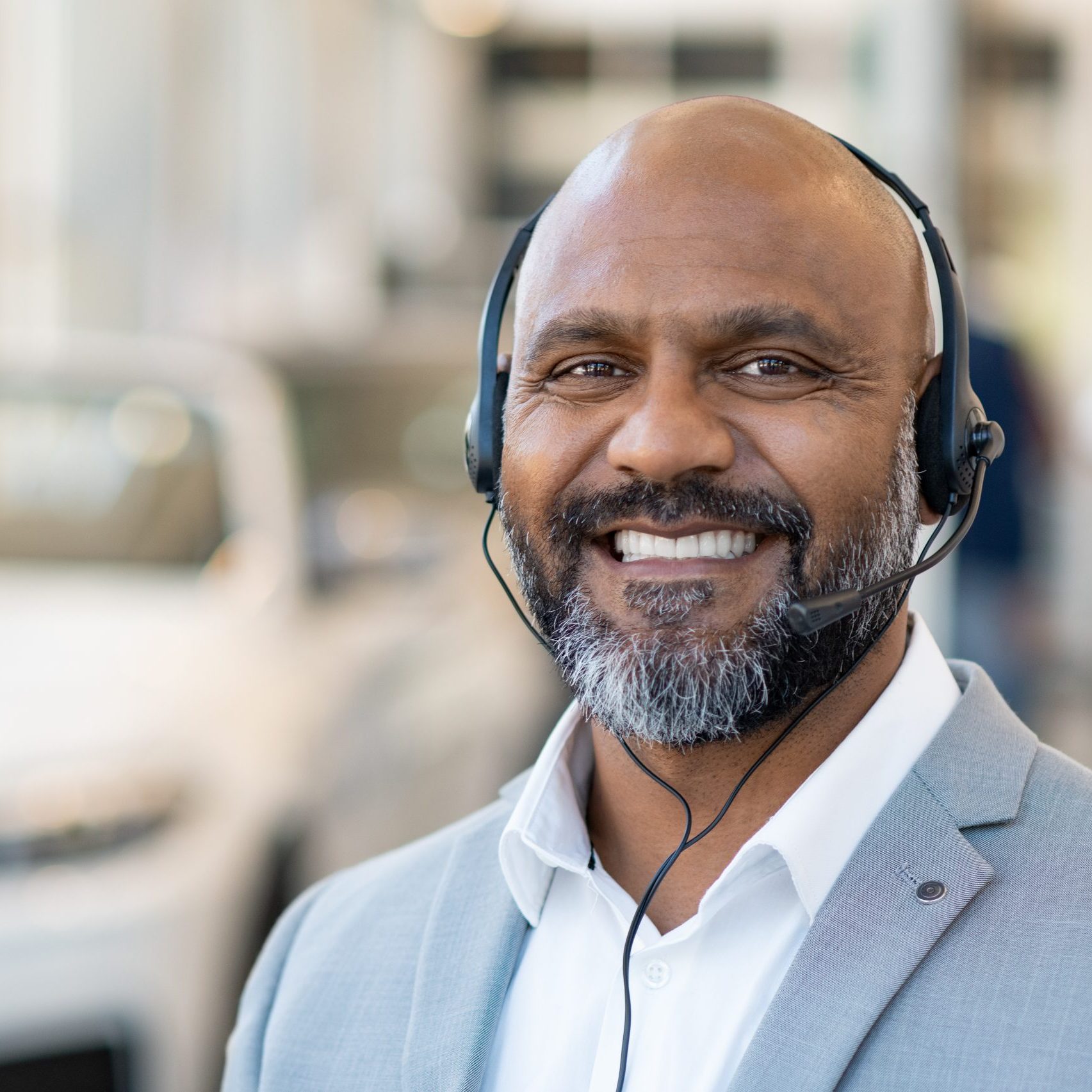 Portrait of mature african consultant man of call center with headset smiling and looking at camera in car showroom. Happy smiling customer support working with headset. Smiling car dealer after sales telephone assistance.