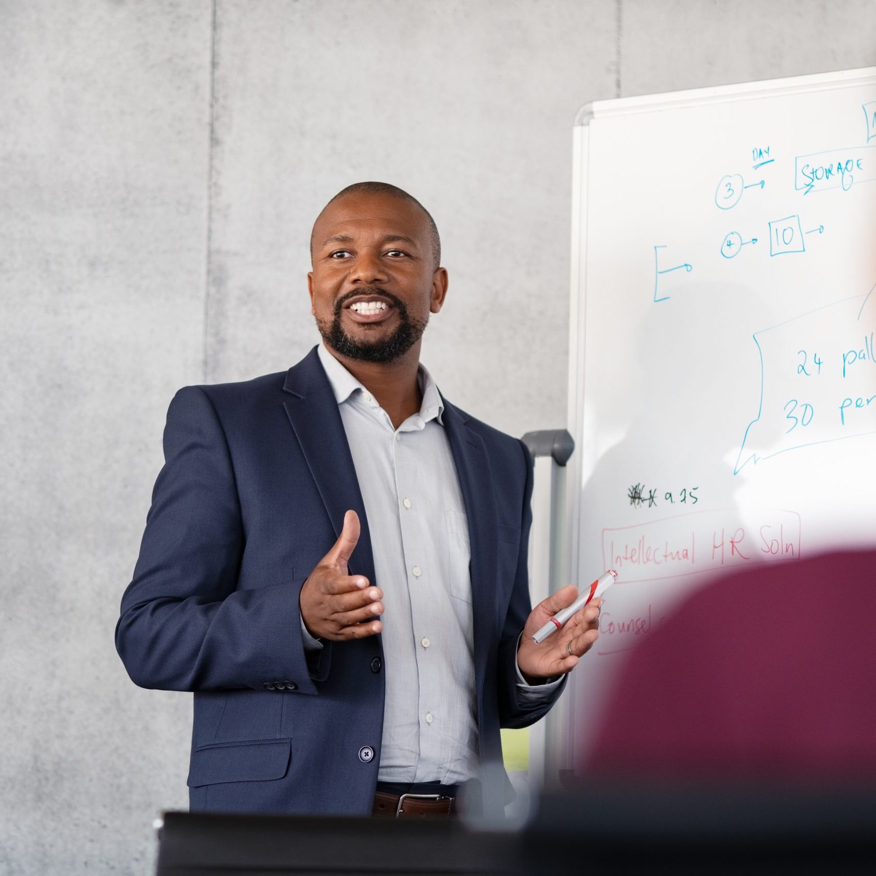 Mature african american coach explaining strategy to his team with copy space. Successful businessman presenting new project to employees during meeting room. Conference speaker talk to audience while giving presentation on whiteboard to business group of people.